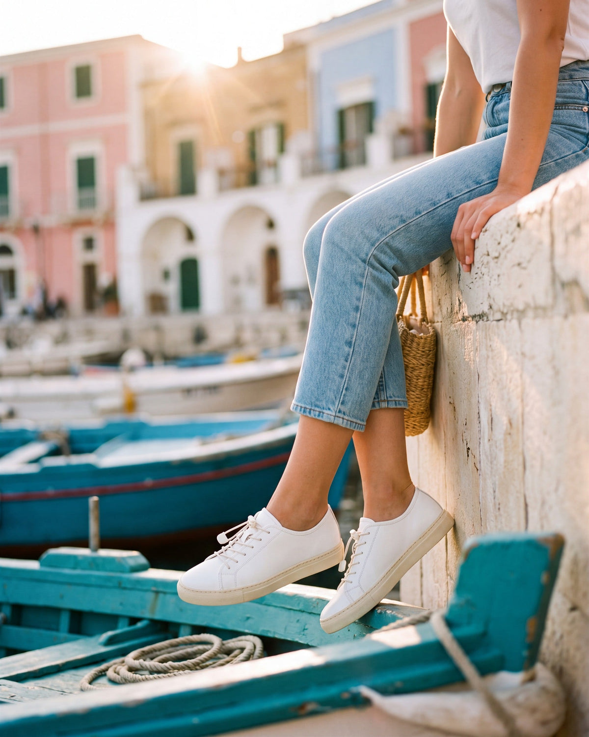 Scarpe - sneakers bianche sul muretto di un porto italiano al tramonto